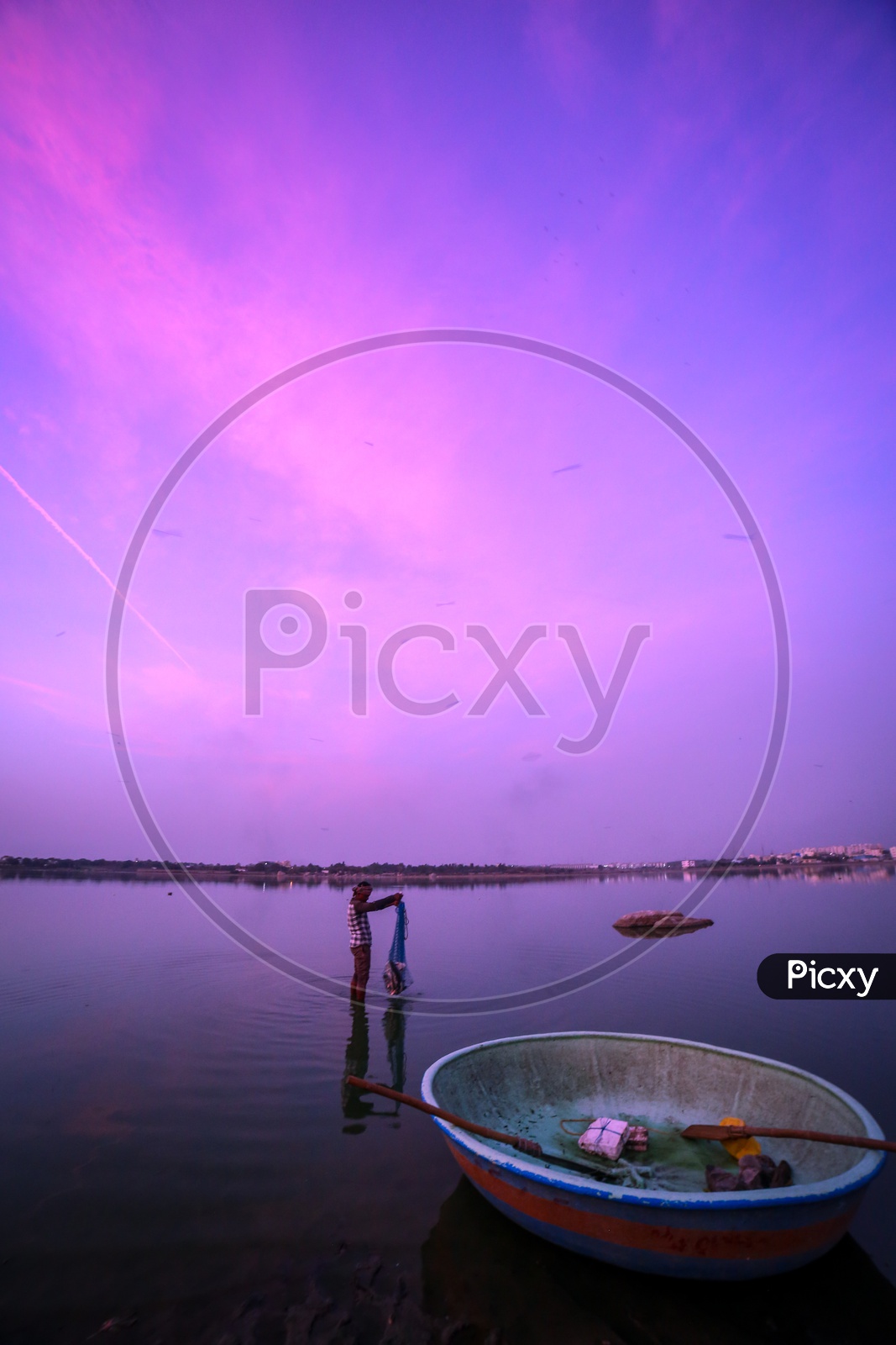 A Fisherman With Fishing Net In a Lake With a Blue Hour Sky Background
