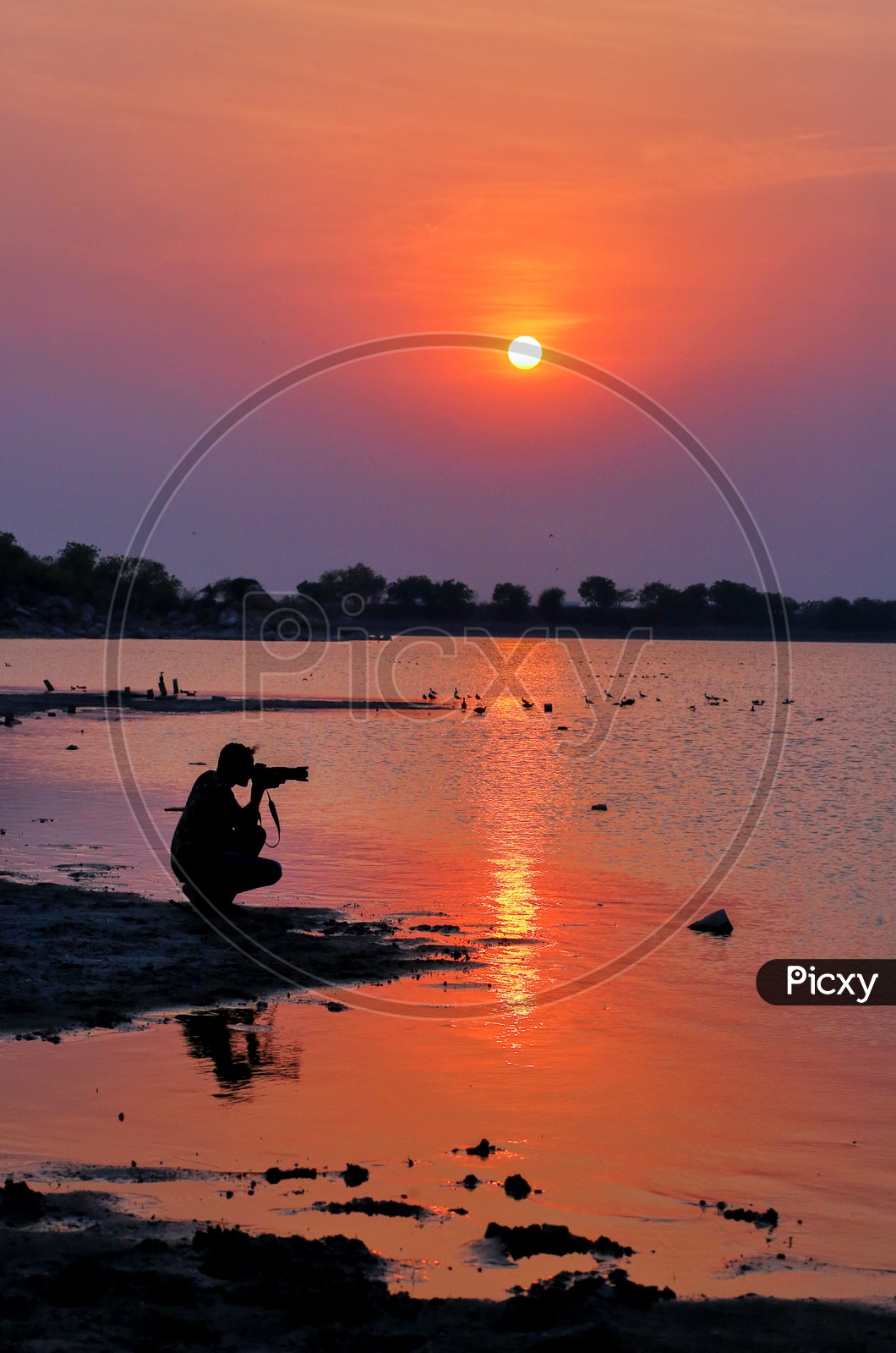 Silhouette Of a Photographer Shooting At Bank Of a Lake With Sunset Sky In Background
