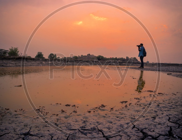 A Photographer And His Reflection On Water With a Sunset Sky In Background