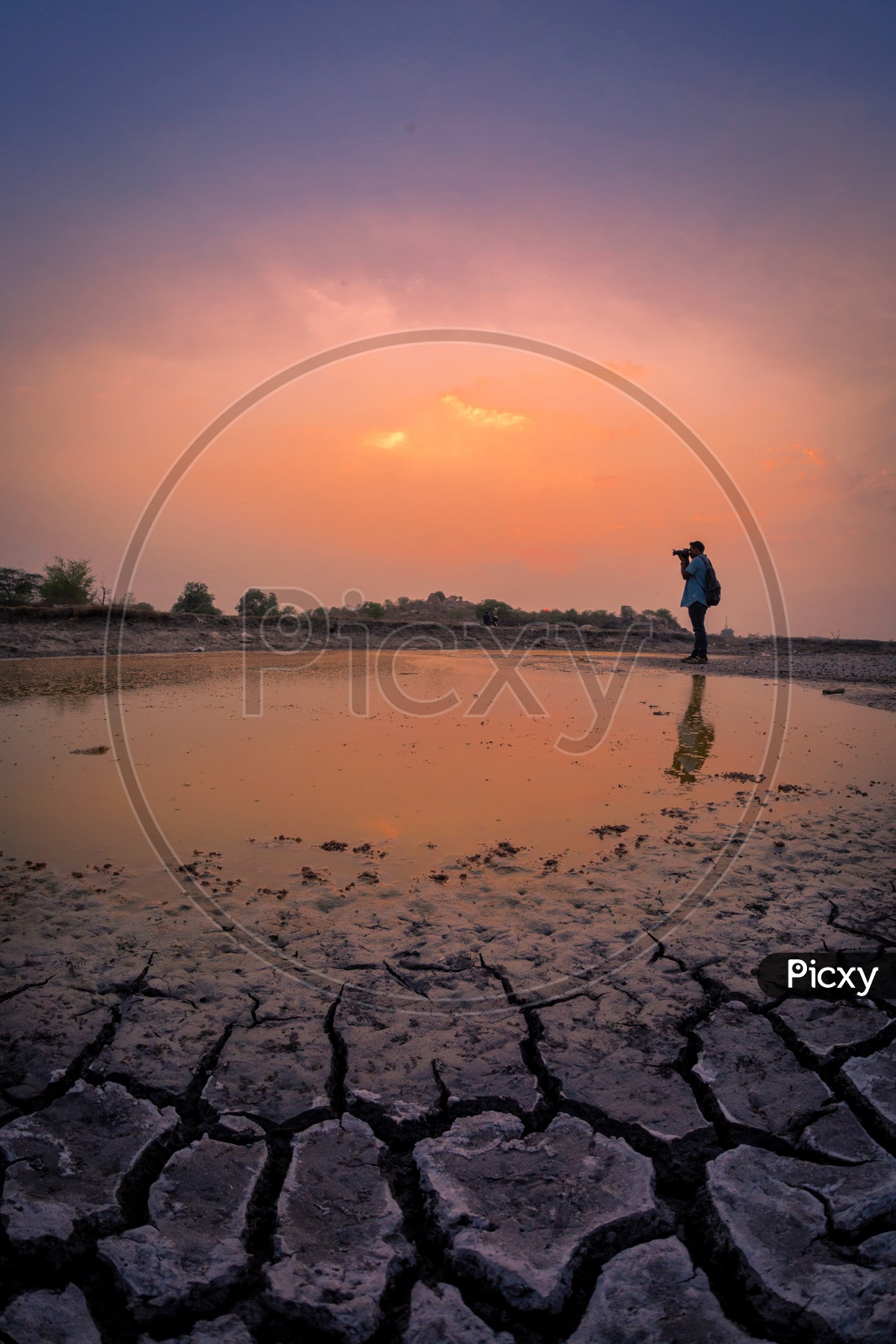 A Photographer And His Reflection On Water With a Sunset Sky In Background