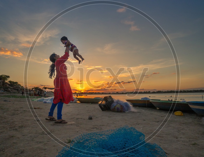 A Mother Playing With Her Child At The Bank Of a Lake  With Sunset Sky In Background