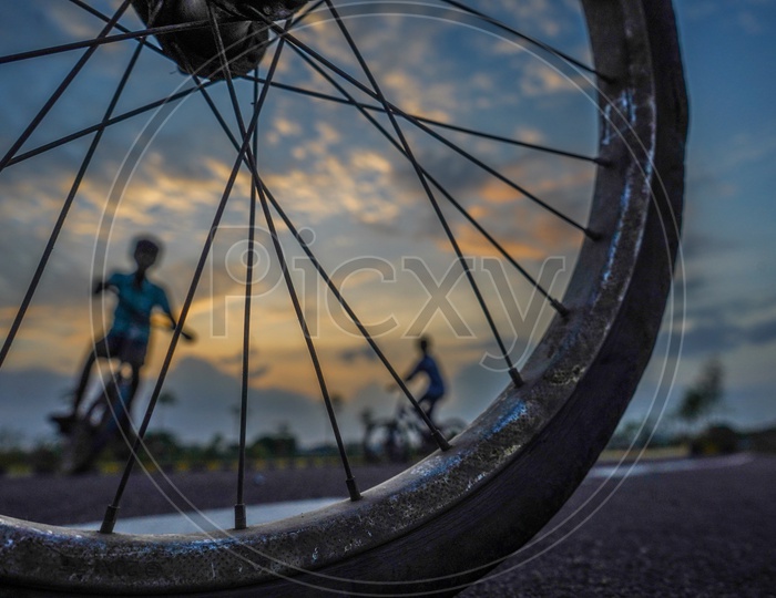 Composition Shot of Happy Or Joyful Indian Young Boys Performing Bicycle Stunts  With Closeup Of Tyre And Folks