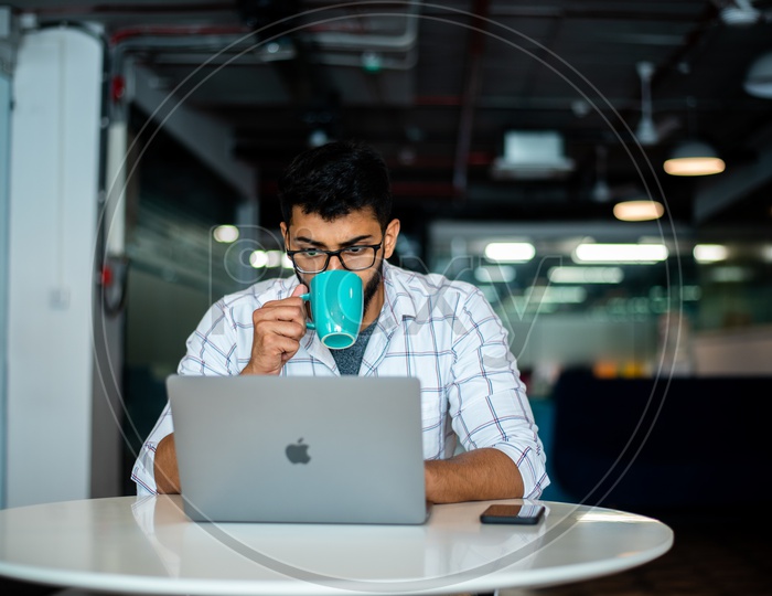 Stressed Young Man Or Indian Man Having Coffee While Working On Laptop  at Work Space