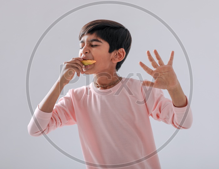 Indian Cute Boy  or  Asian Boy or kid Enjoy Eating  Mango With an Expression On an Isolated White Background