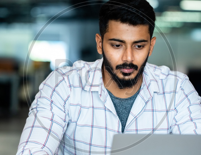 Focused Serious Working Indian Professional Employee  Young Man  On Laptop In Office Work Space