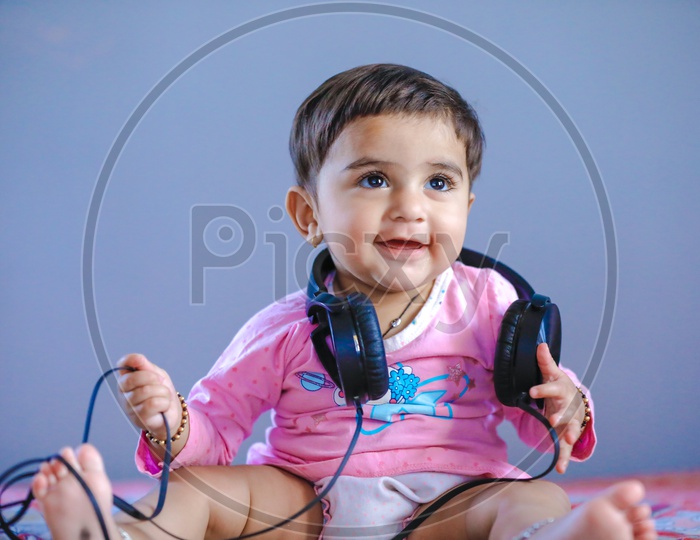 Cute Indian Baby Girl Listening Music  In Headphones With Cute Expressions On Face