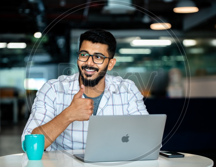 Confident Indian IT Professional  Young Man Employee Student   With Thump Up Gesture Happily Smiling With Laptop on Desk