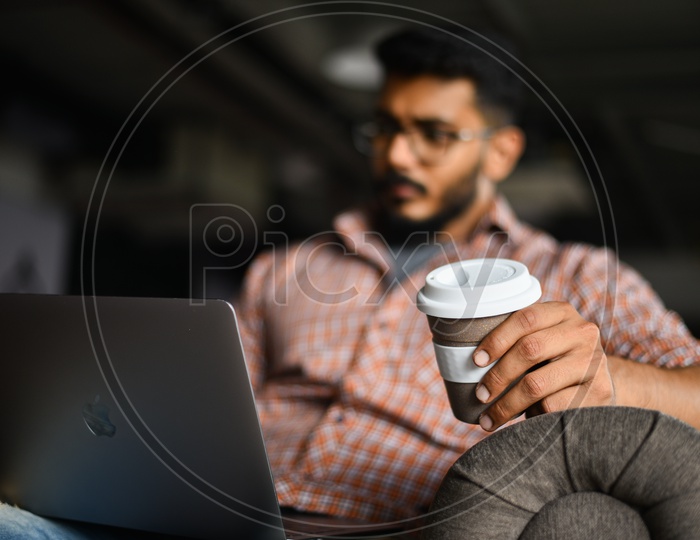 Focused Serious Working Young Man Or Indian Man On Laptop  in a Office Space  With a Coffee Cup In Hand