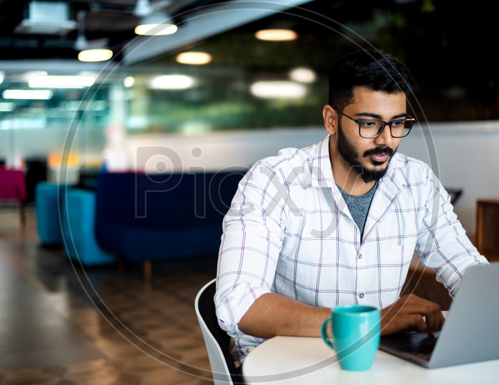 Focused Serious Working Indian Professional IT Employee Young Man Student  On Laptop In Office Work Space