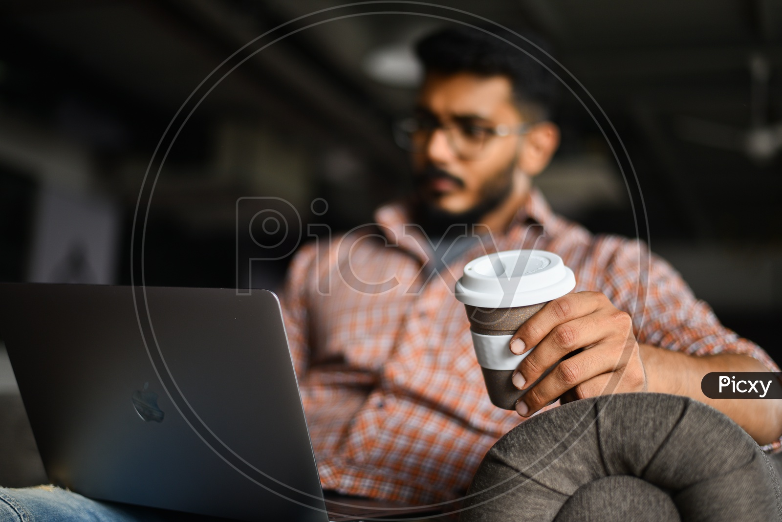 Focused Serious Working Young Man Or Indian Man On Laptop  in a Office Space  With a Coffee Cup In Hand