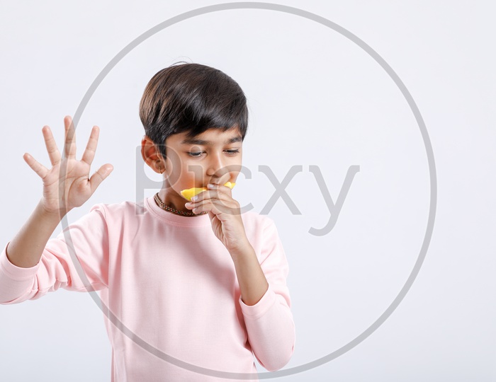 Indian Cute Boy  or Asian Boy or kid Enjoying Eating  Mango With an Expression On an Isolated White Background