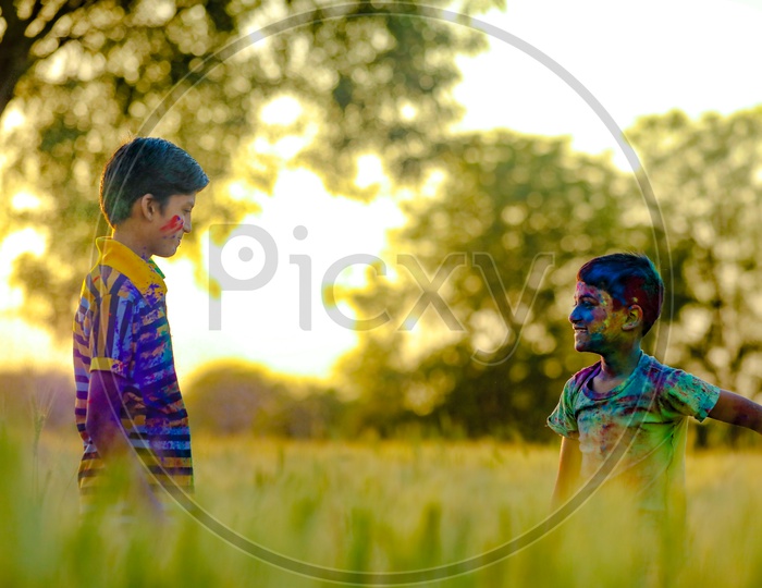 Young Indian Boys Or Brothers Filled In  Holi Colours Playing in a Green  Fields in rural Village Backdrop
