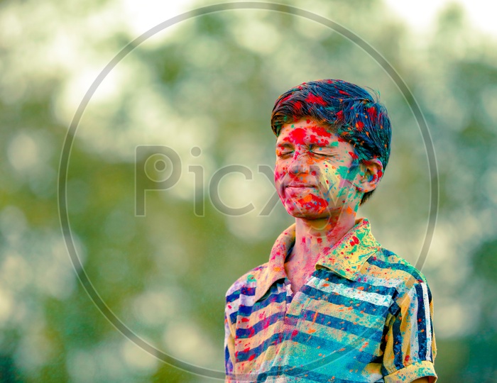 Indian Boy or Young Indian Boy Child  Playing Or Filled In Holi Colours Celebrating Holi Festival in Green Fields Background