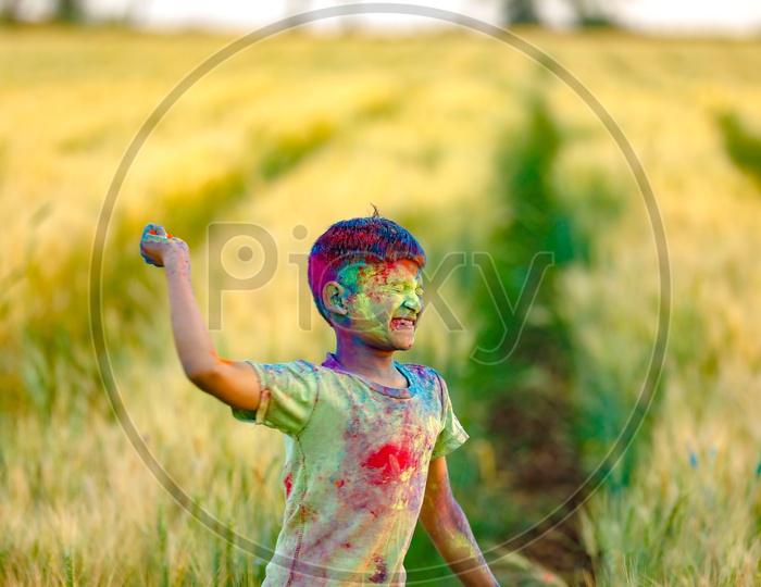 Indian Boy or Young Indian Boy  Playing Or Filled In Holi Colours Celebrating Holi Festival in Green Fields Background