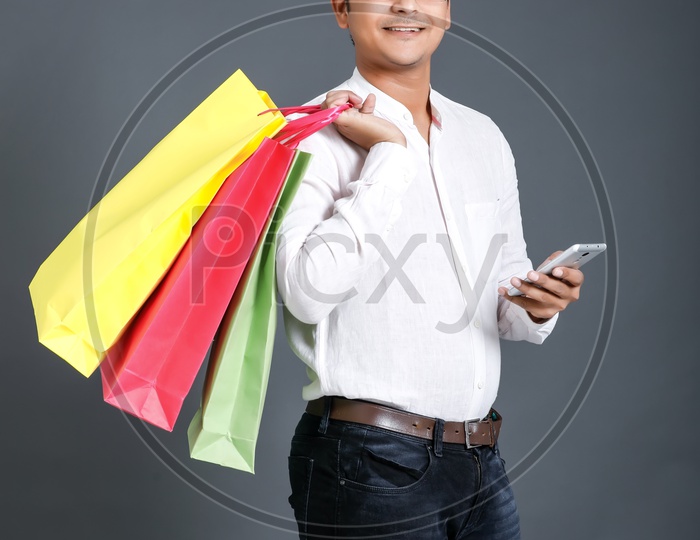 Young Man Carrying  Shopping Bags  And Using Mobile Or Smart Phone Over an Isolated Black Background