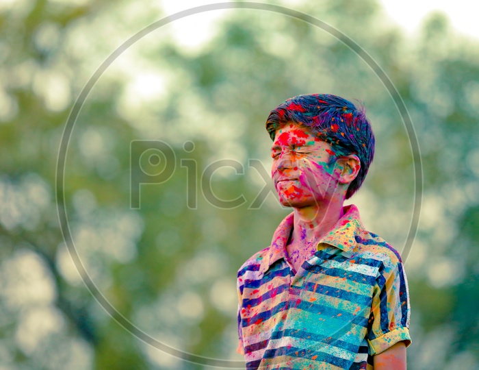 Indian Boy or Young Indian Boy Child  Playing Or Filled In Holi Colours Celebrating Holi Festival in Green Fields Background