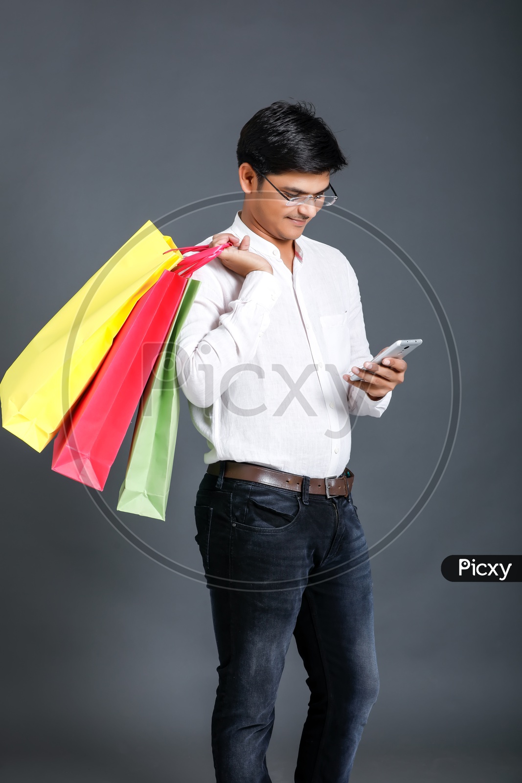 Young Man Carrying  Shopping Bags  And Using Mobile Or Smart Phone Over an Isolated Black Background