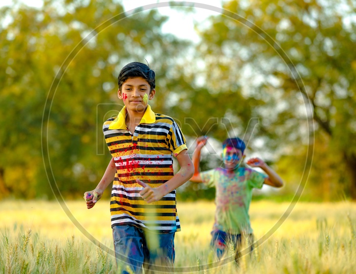 Young Indian Boys Or Brothers Filled In  Holi Colours Playing in a Green  Fields in rural Village Backdrop
