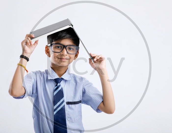 Indian or Asian Kid Or Boy  Or Student In School Uniform And Book On Head Over an Isolated White Background