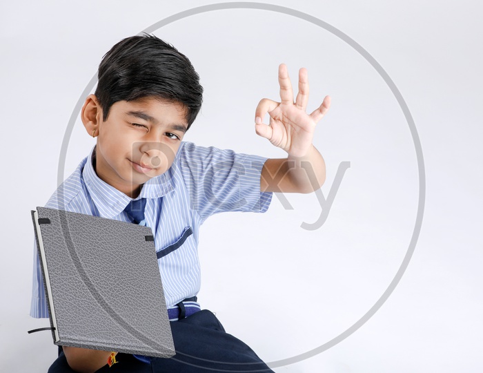 Indian Or Asian Kid Or Boy Or Student   In School Uniform  Holding a Book And Posing Over an Isolate White Background