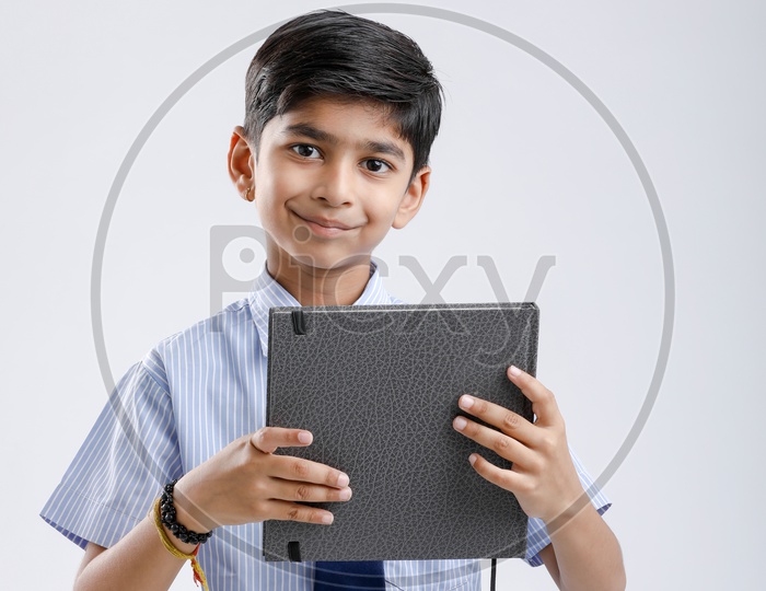 Indian or Asian Kid Or Boy Or Student  In School Uniform And Holding Book Over an Isolated White Background