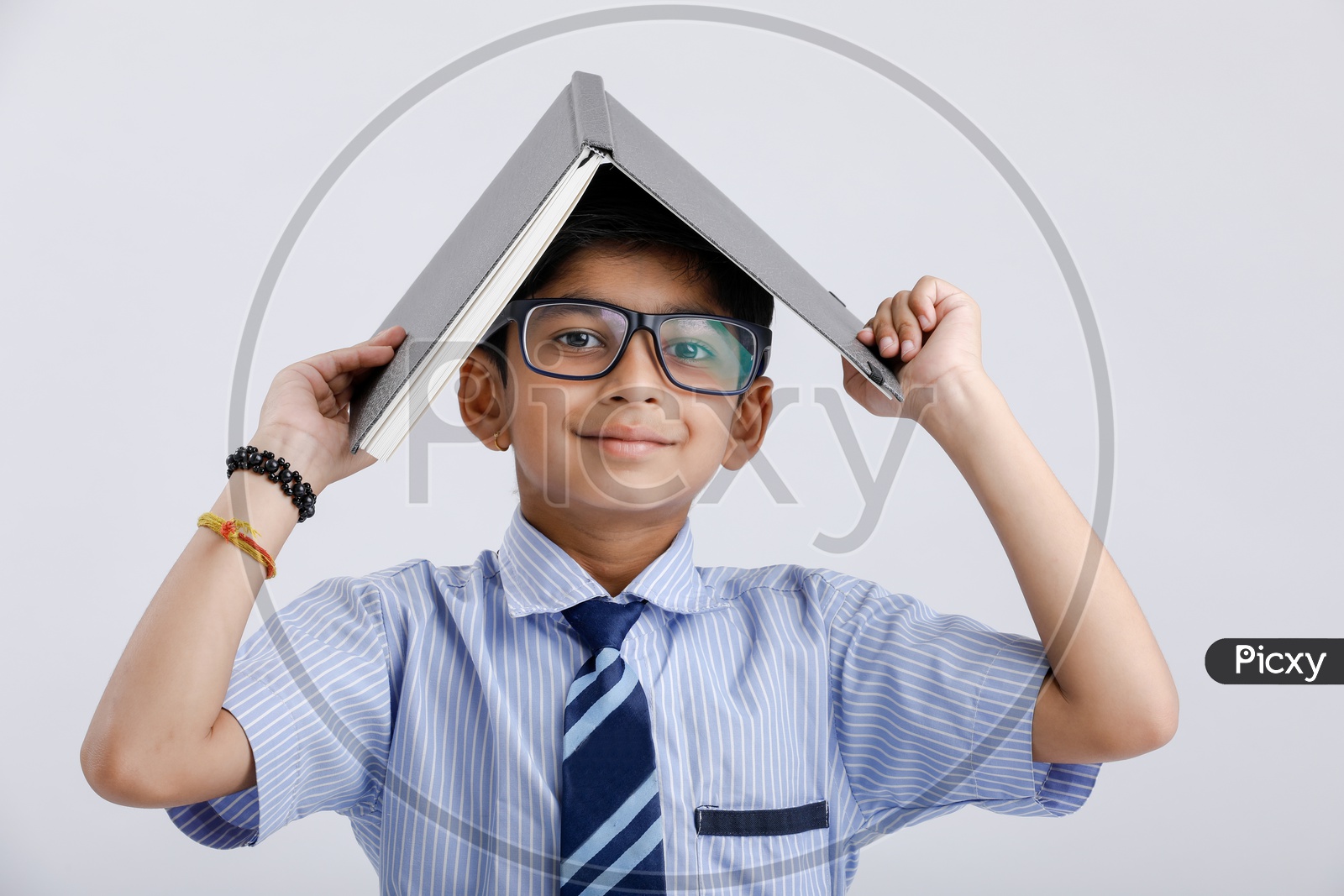 Indian Or Asian Boy Or Kid Or student in School Uniform  Wearing Spectacles And Book On Head Posing Over an Isolated White Background