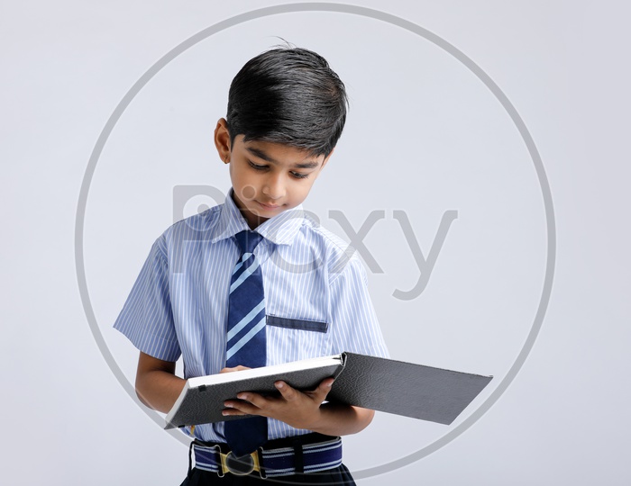Cute Indian or Asian Kid Or Boy In School Uniform And Reading Book   Over an Isolated White Background