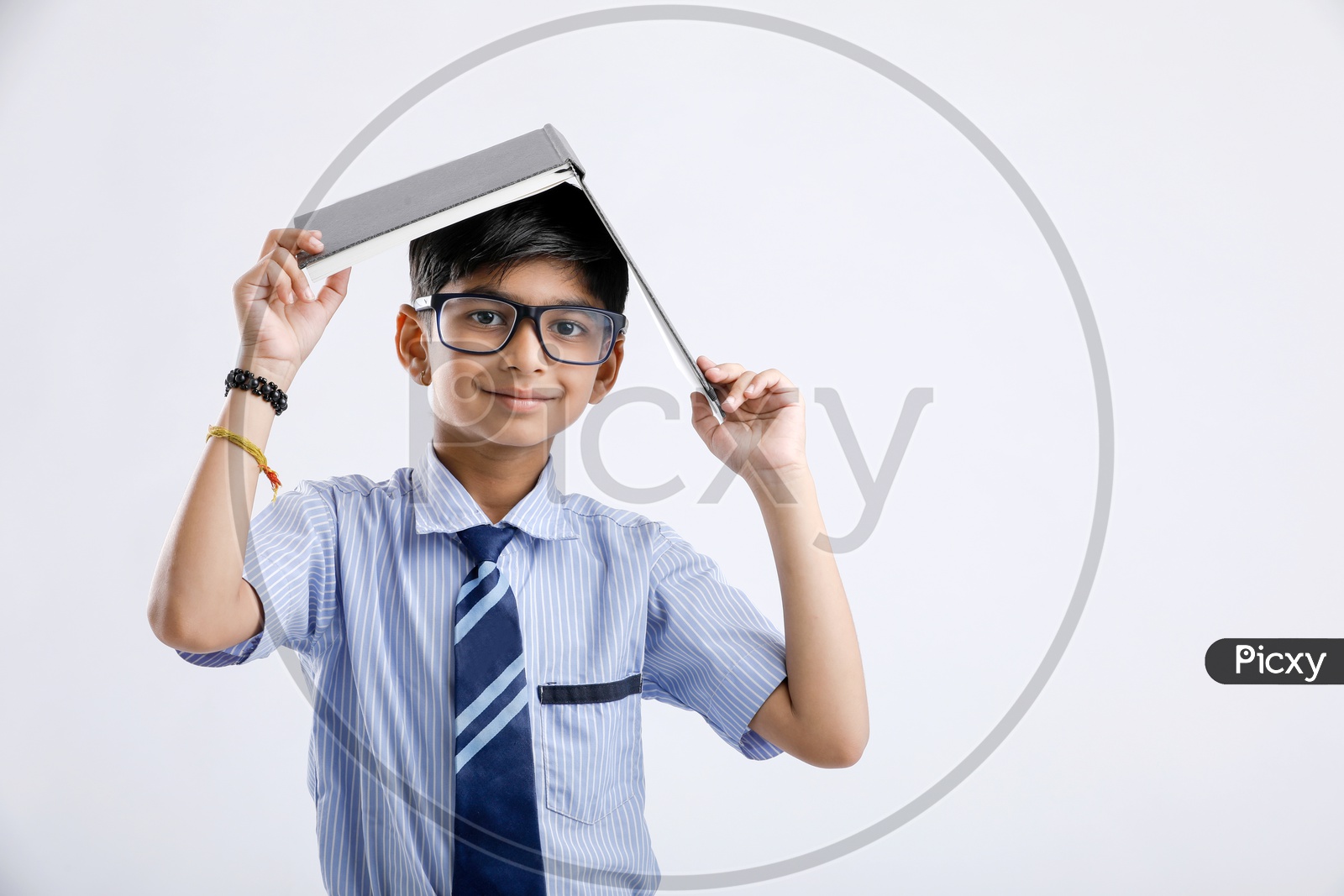 Indian or Asian Kid Or Boy  Or Student In School Uniform And Book On Head Over an Isolated White Background