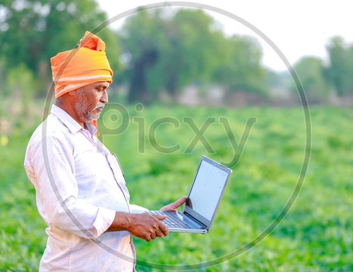 Indian Farmer Using Laptop On Green Farm Fields Background