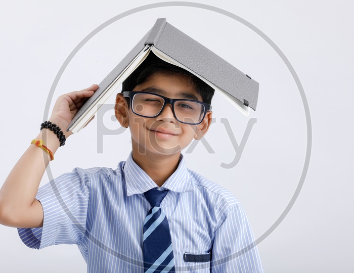 Indian Or Asian Boy Or Kid Or student in School Uniform  Wearing Spectacles And Book On Head Posing Over an Isolated White Background