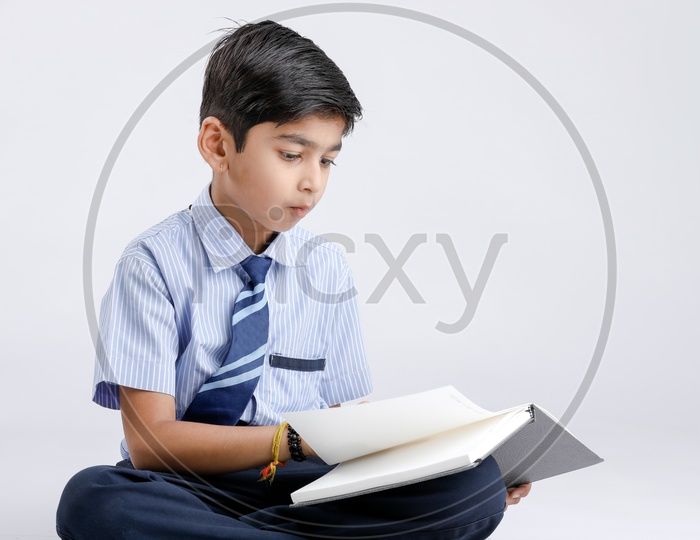 Cute Indian or Asian Kid Or Boy In School Uniform And Reading  Book   Over an Isolated White Background