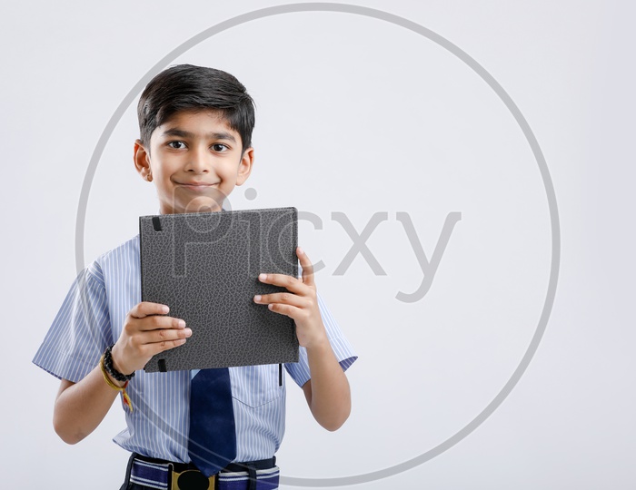Cute Indian or Asian Kid Or Boy In School Uniform And Holding  Book   Over an Isolated White Background