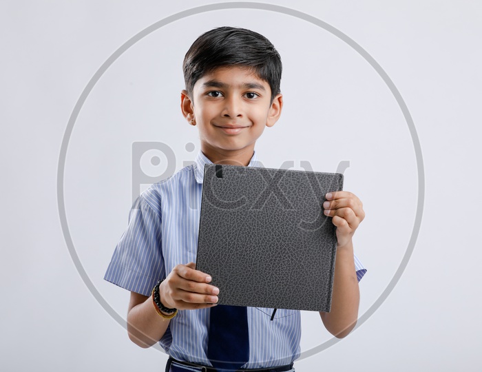 Indian or Asian Kid Or Boy  Or Student In School Uniform And  Holding  Book   Over an Isolated White Background