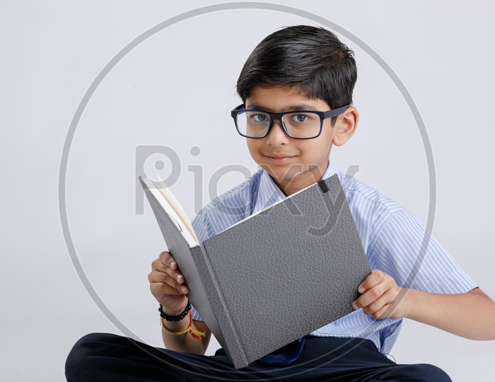Indian Or Asian Boy Or Kid Or student in School Uniform  Wearing Spectacles And  Reading Book  Over an Isolated White Background