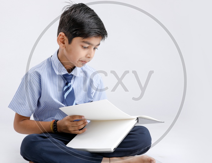 Cute Indian or Asian Kid Or Boy In School Uniform And Reading  Book   Over an Isolated White Background