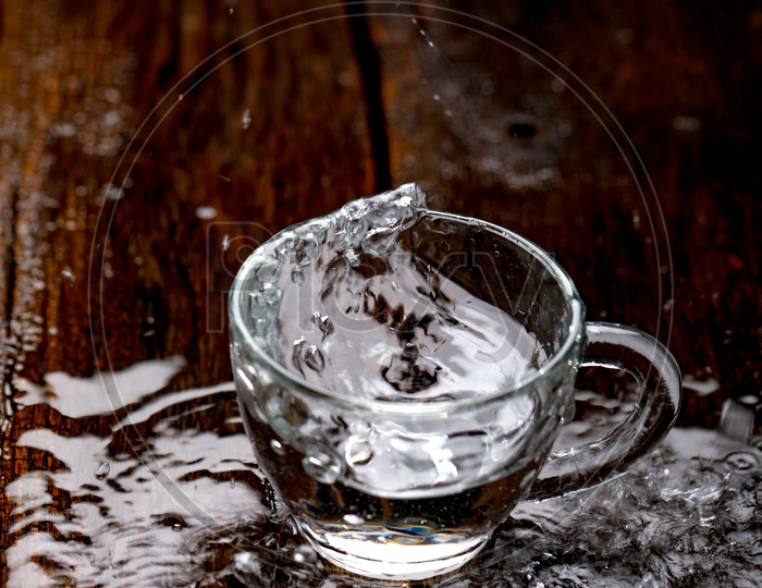 Glass Tea Cup Filling With Water With Water Splash On an Wooden Background