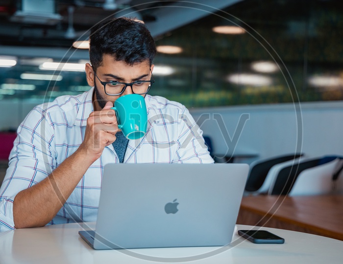 Stressed Tired  Indian professional Young  Man  Having Coffee While Working On Laptop  at Work Space