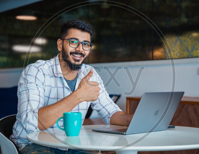Confident Young Man or Indian Man Or Student With Thump Up Gesture Happily Smiling With Laptop on  Office  Desk
