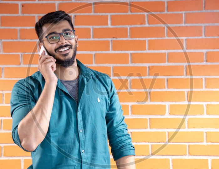 Young Man Or  Student  Speaking Or Talking In Smartphone or Mobile  With a Smile Face  Over  A Brick wall  Background