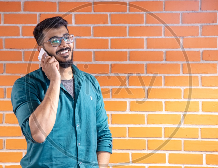 Young Man Or  Student  Speaking Or Talking In Smartphone  or Mobile With a Smile Face  Over  A Brick wall  Background