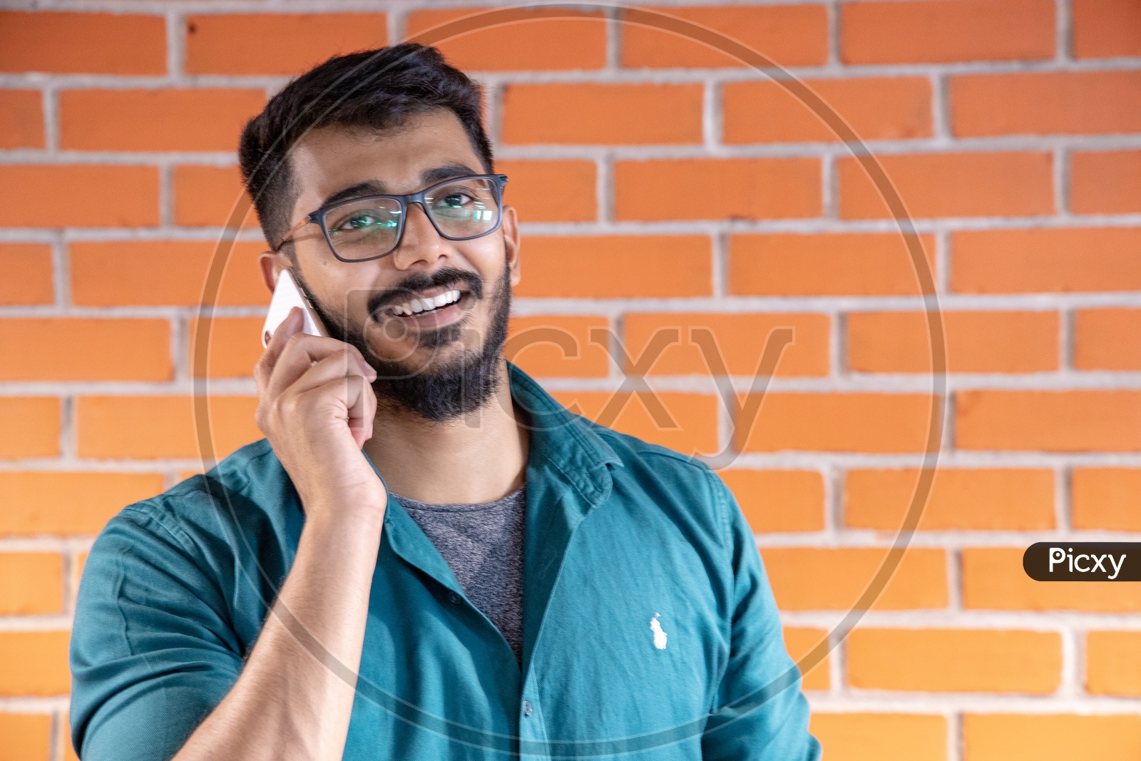 Young Man Or  Student  Speaking Or Talking In Smartphone or Mobile With a Smile Face  Over  A Brick wall  Background