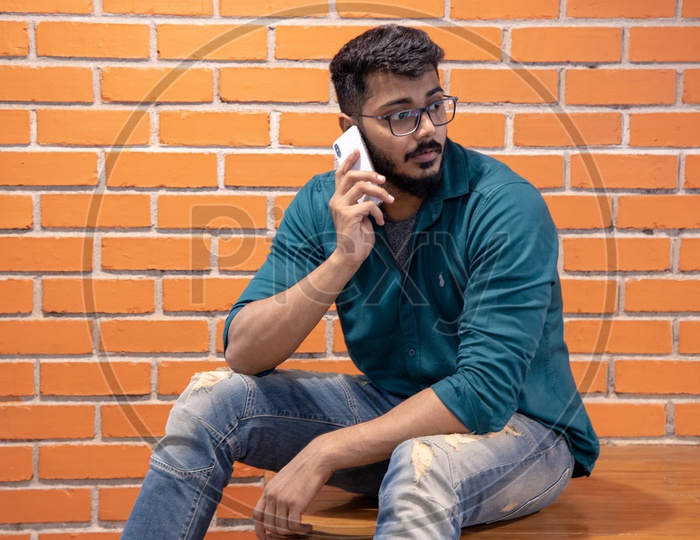 Young Man Or  Student  Speaking Or Talking In Smartphone or Mobile   Over  A Brick wall  Background