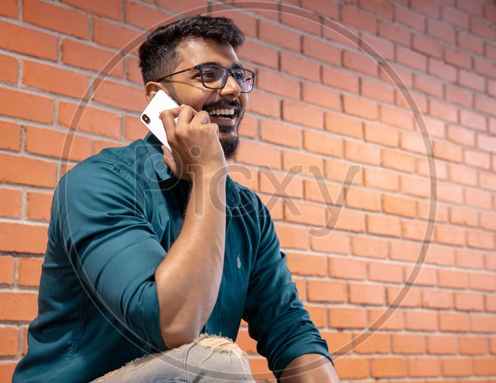 Young Man Or  Student  Speaking Or Talking In Smartphone  or Mobile With a Smile Face  Over  A Brick wall  Background