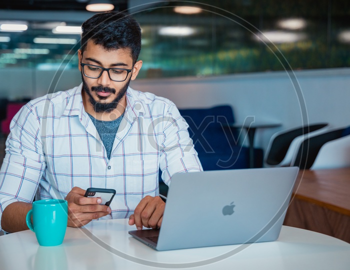 Young Man Or Indian Man or Student Using  Mobile Or Smartphone  At Work Space With Laptop on Desk