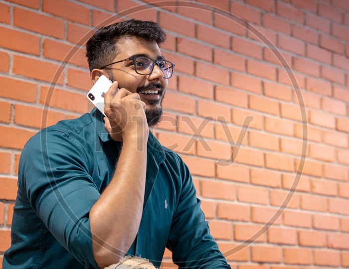 Young Man Or  Student  Speaking Or Talking In Smartphone With a Smile Face  Over  A Brick wall  Background