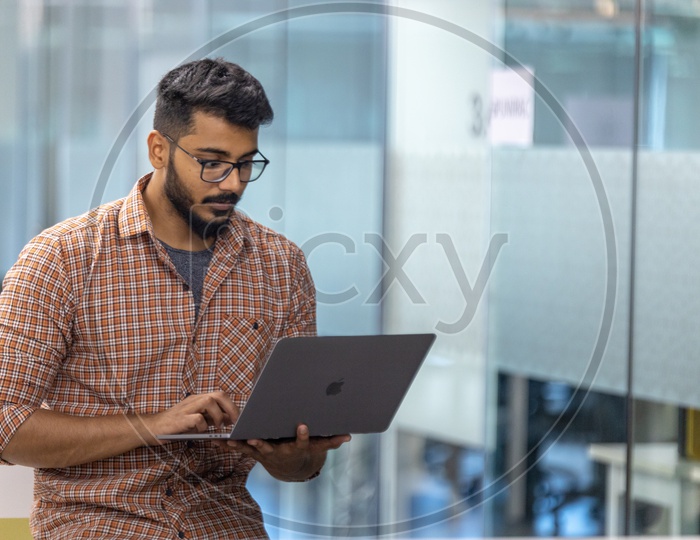Focused Serious Working Young Man Or Indian Man On Laptop   In Office Work Space  Background