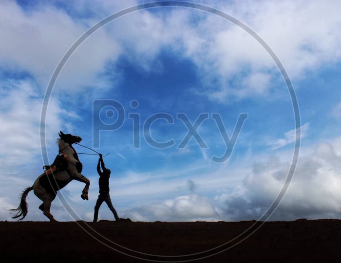 A horse rider training his horse with a backdrop of cloudscape at Mahabaleshwar