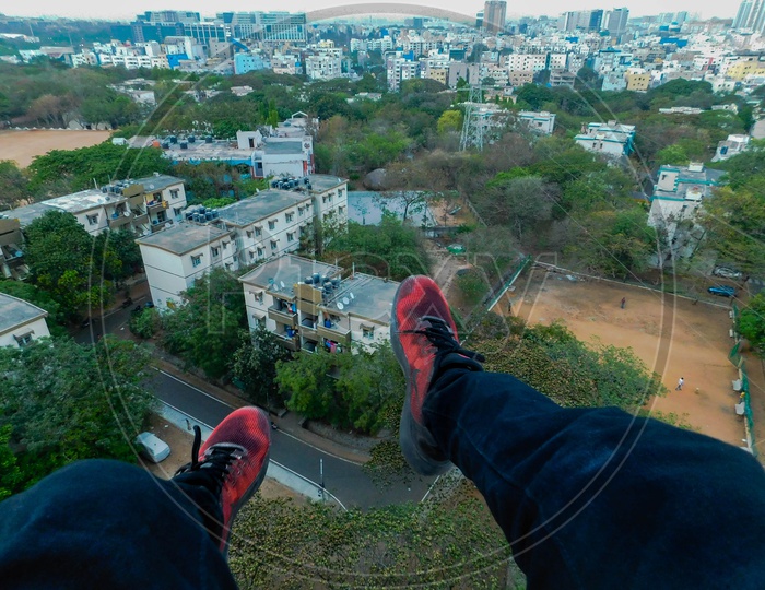 Legs hanging in the air from a tall building and a city view