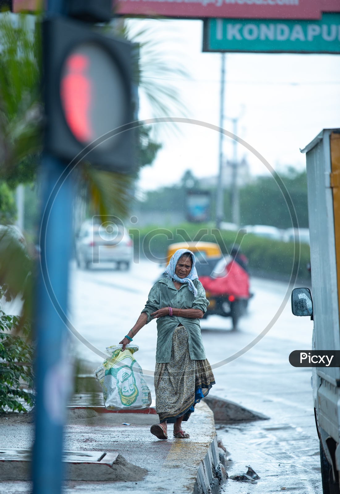 A Rag Picker Walking With a Collection Bag On Hi-tech City Footpaths  in Rain Drizzle