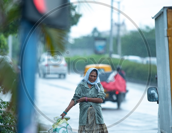 A Rag Picker Walking With a Collection Bag On Hi-tech City Footpaths  in Rain Drizzle